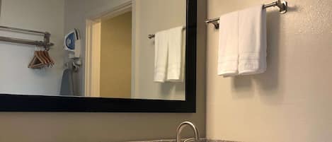 A bathroom with a granite countertop, a white sink, a mirror with three lights, and a towel rack with two white towels.