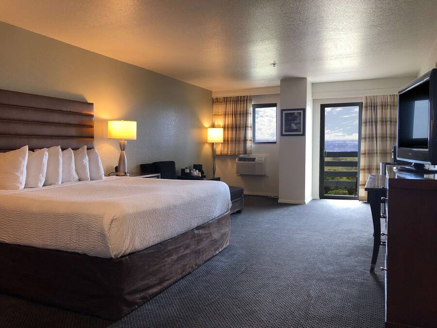 A hotel room with a large bed, two bedside lamps, a desk with a television, and a window with a view.