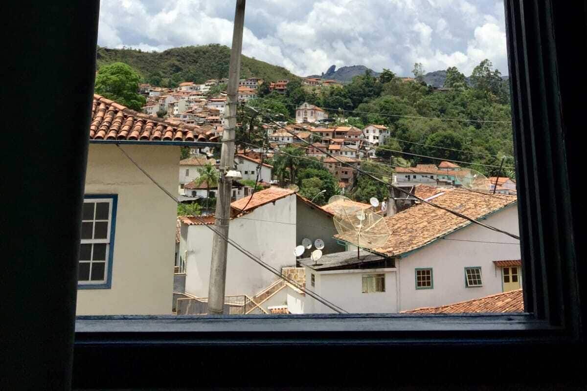 Una ventana con vistas a un pueblo en la ladera, con edificios de tejados de teja.