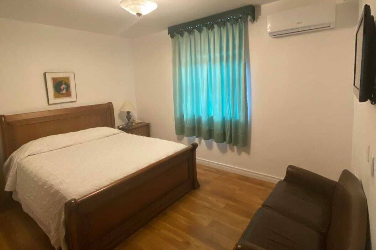 Un dormitorio con cama de madera, mesita de noche, aire acondicionado instalado en la pared y ventana con cortinas turquesa.