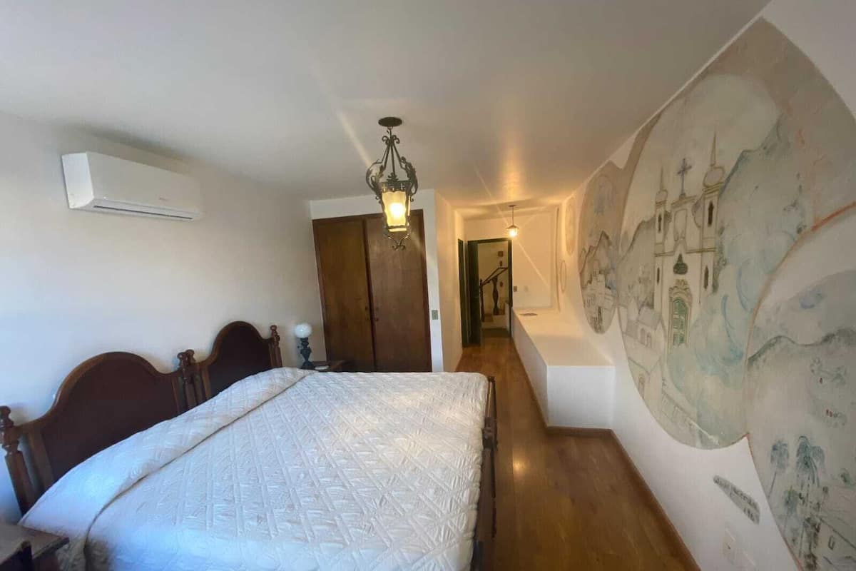 Un dormitorio con una cama grande, cabecera de madera, aire acondicionado montado en la pared, una araña y un mural en la pared.
