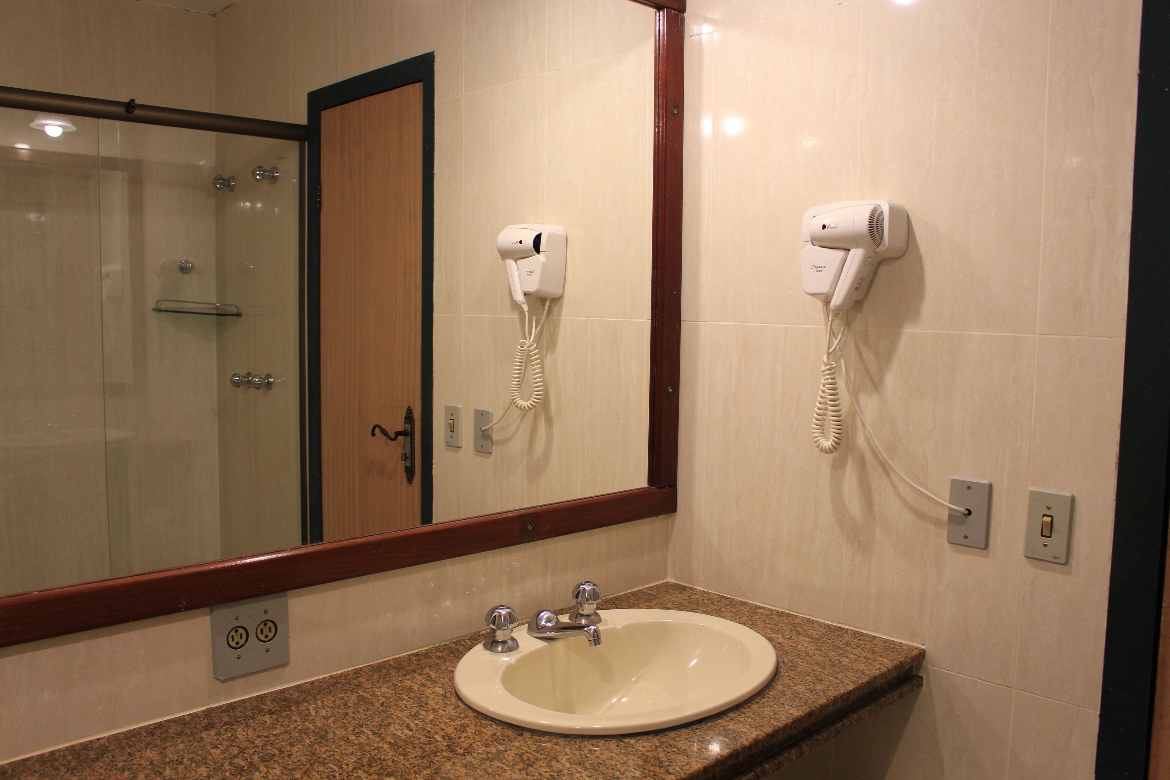 A bathroom with a sink, mirror, and two hair dryers mounted on the wall.