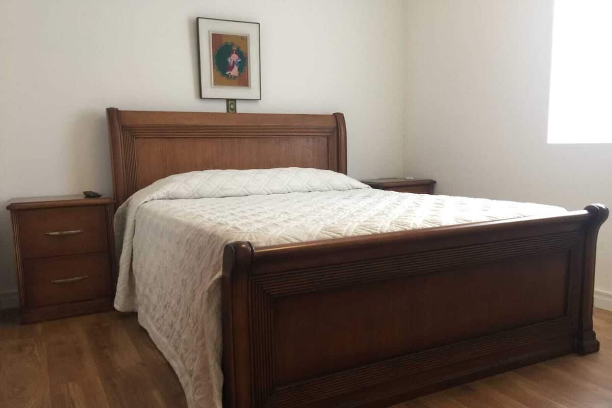 Un dormitorio con cama de madera, mesita de noche, cómoda y un cuadro enmarcado en la pared.