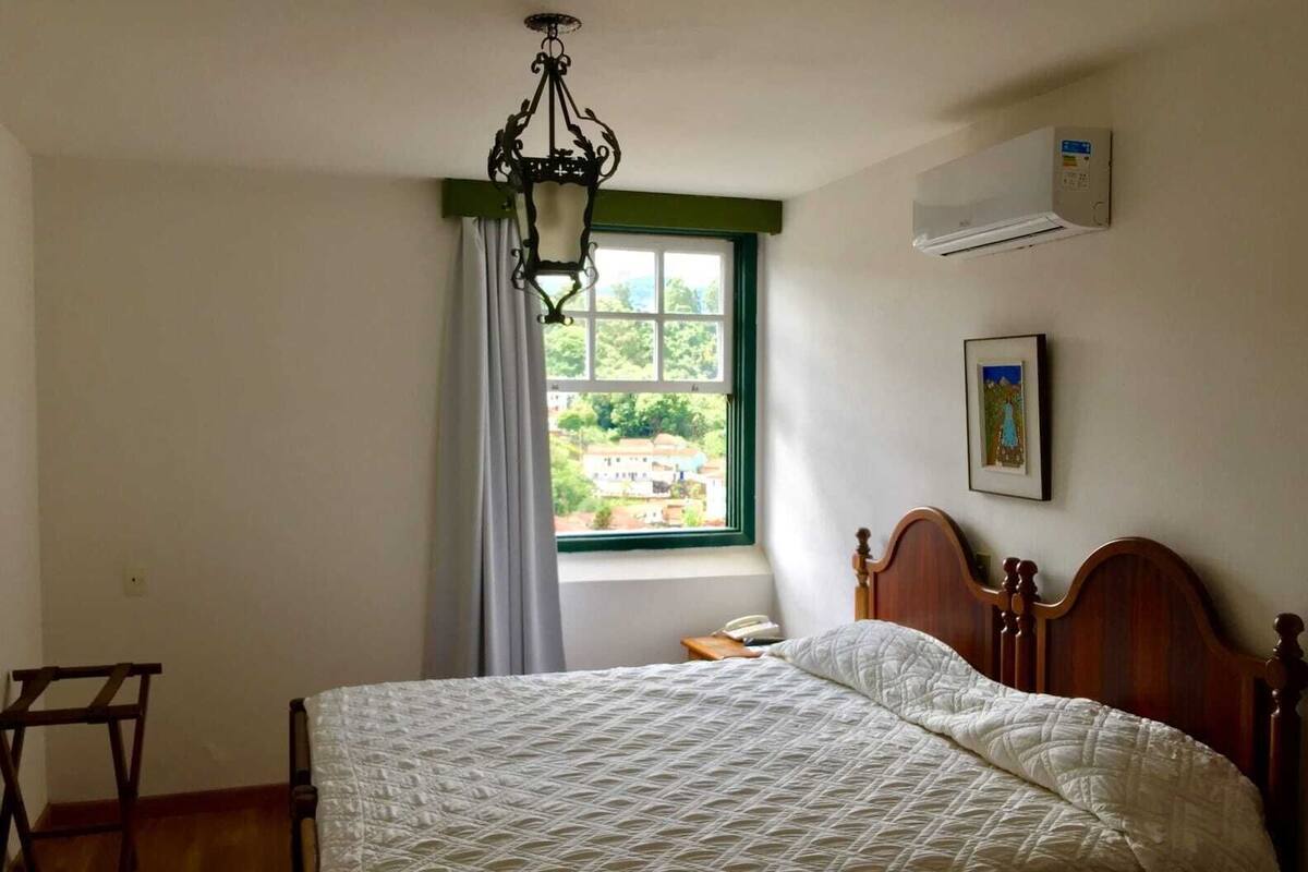 Un dormitorio con una cama de madera, una lámpara colgante, una ventana con cortinas, un aire acondicionado y un cuadro en la pared.