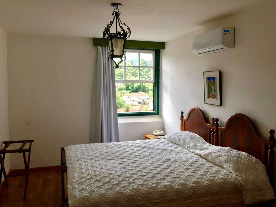 Un dormitorio con una cama de madera, una lámpara colgante, una ventana con cortinas, un aire acondicionado y un cuadro en la pared.