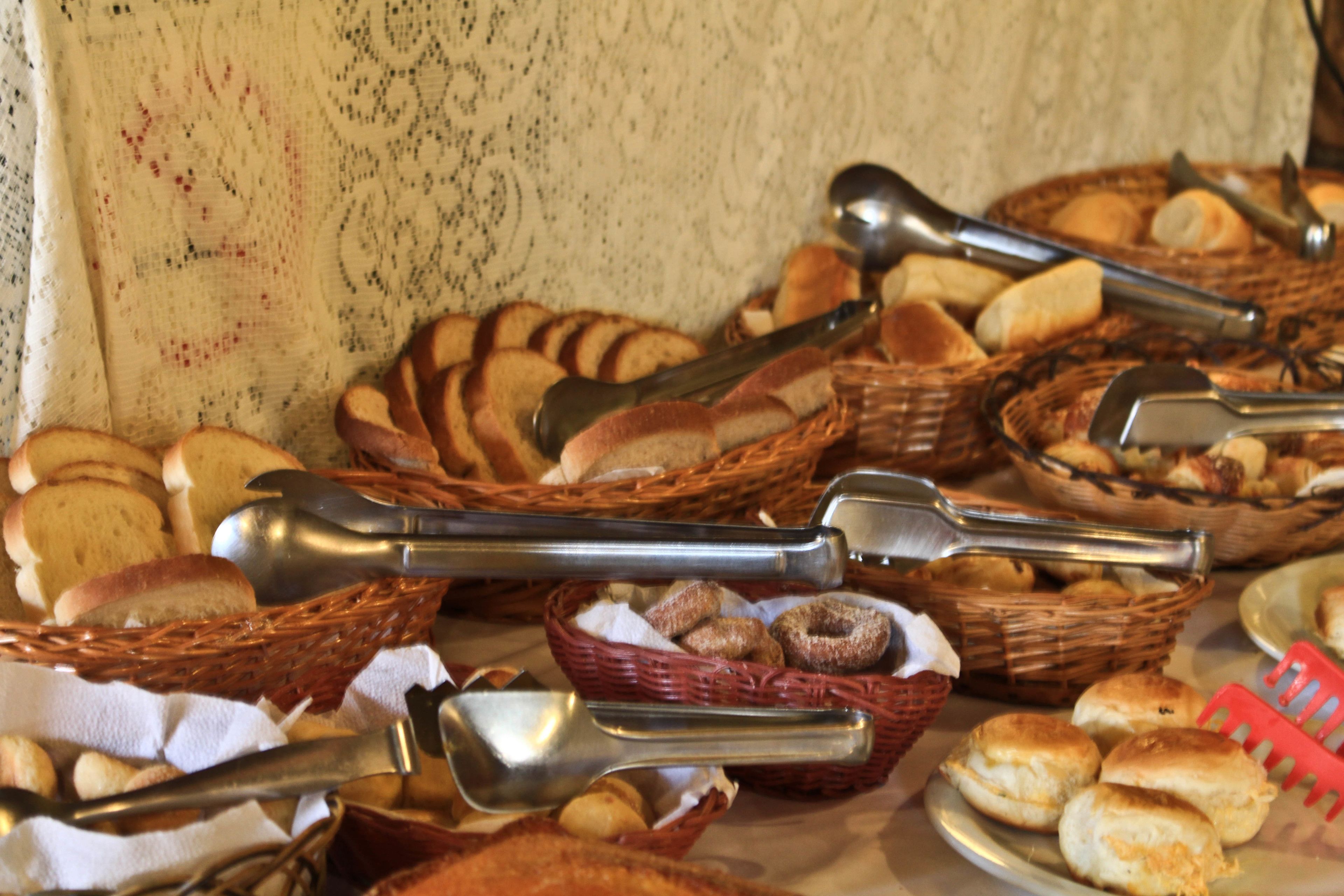 A table with baskets of bread and doughnuts, and tongs for serving.