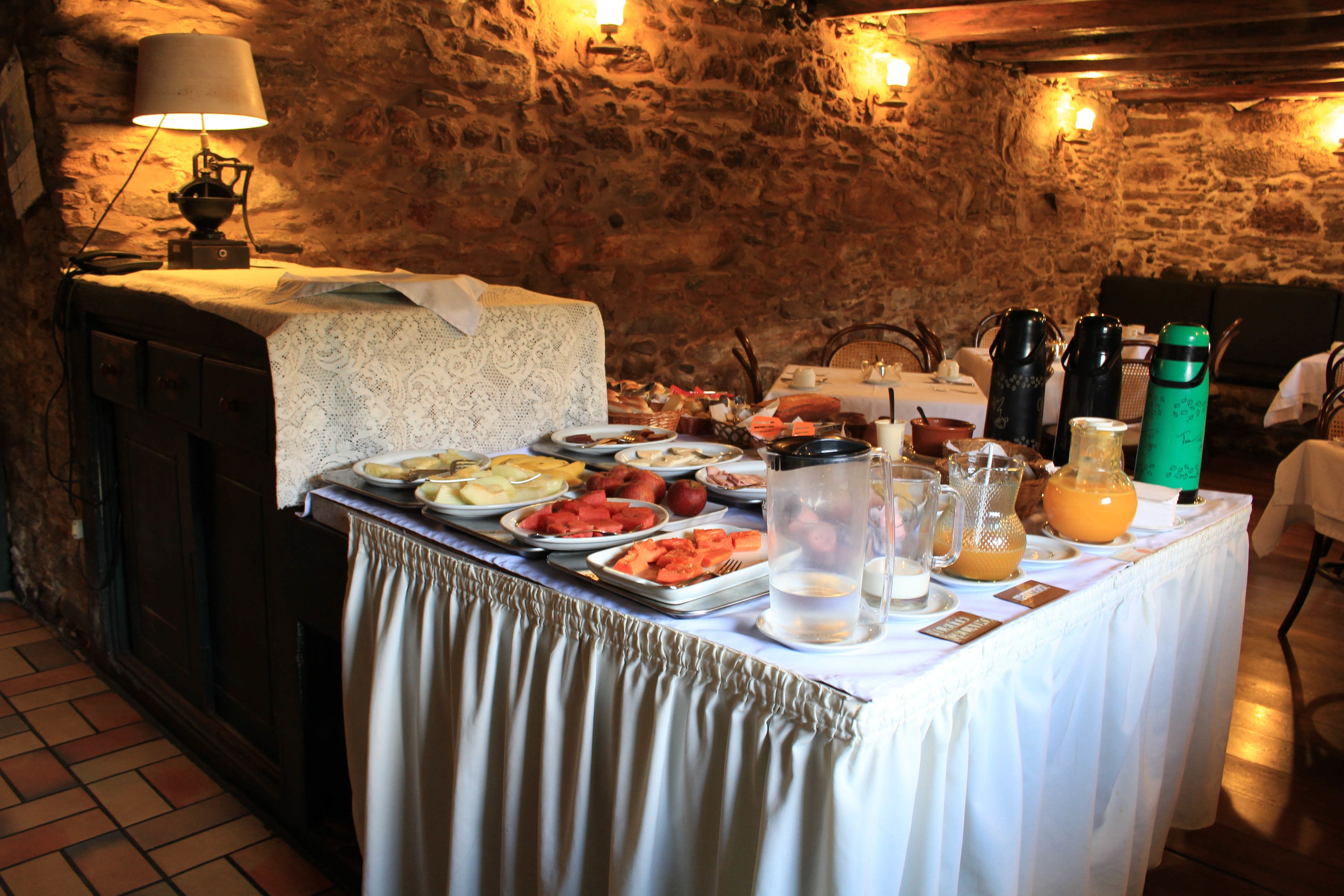 A buffet table with various food items and beverages, set against a stone wall background.