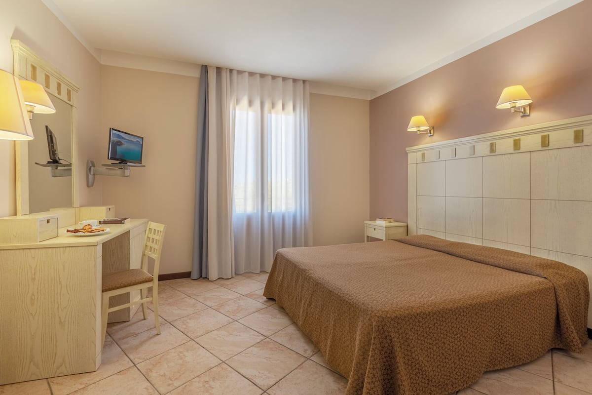 Camera d'albergo con un letto, una scrivania con una sedia, una televisione e una finestra con tende.