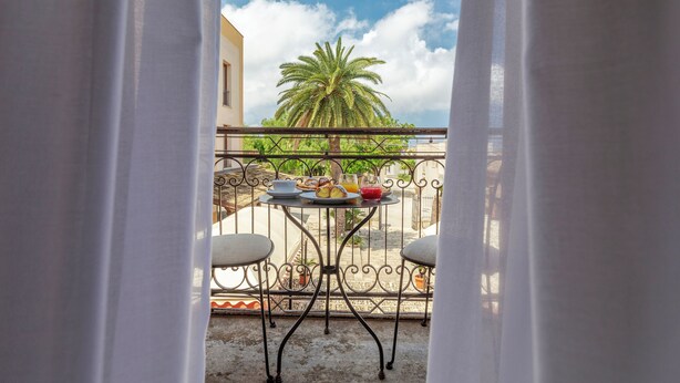 A balcony with a table set for breakfast, a palm tree, and a clear sky.