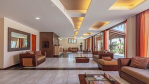 A spacious lobby with a modern design, featuring a central seating area with sofas and a coffee table, a large mirror, and a view of the outdoors through large windows.