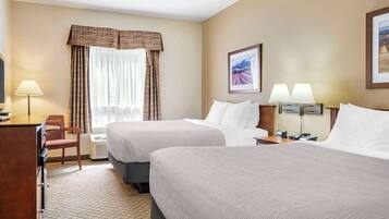 A hotel room with two beds, a desk, a chair, a lamp, and a framed picture on the wall.