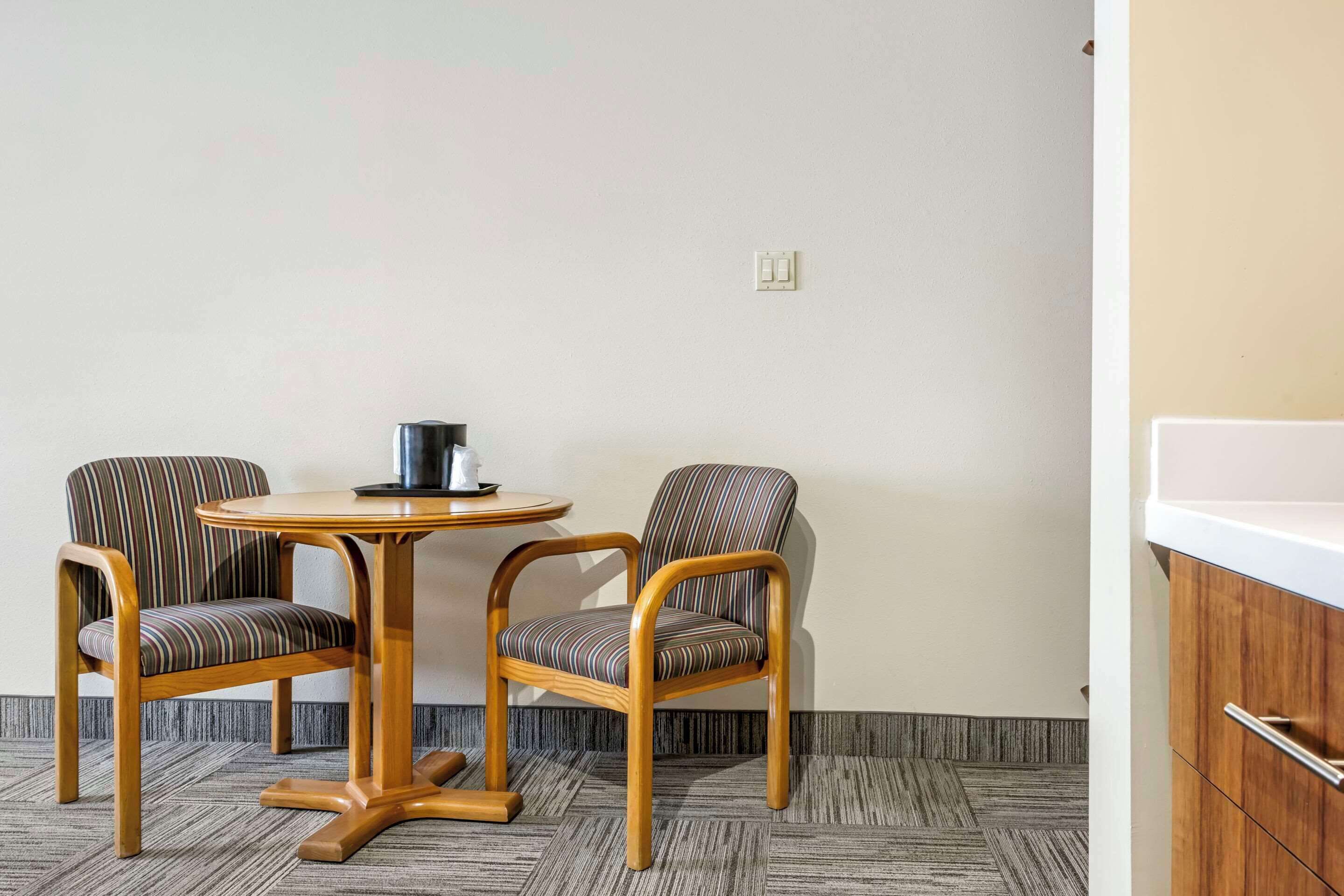 Una habitación con dos sillas a rayas, una mesa redonda, un lavamanos blanco y un armario de madera.
