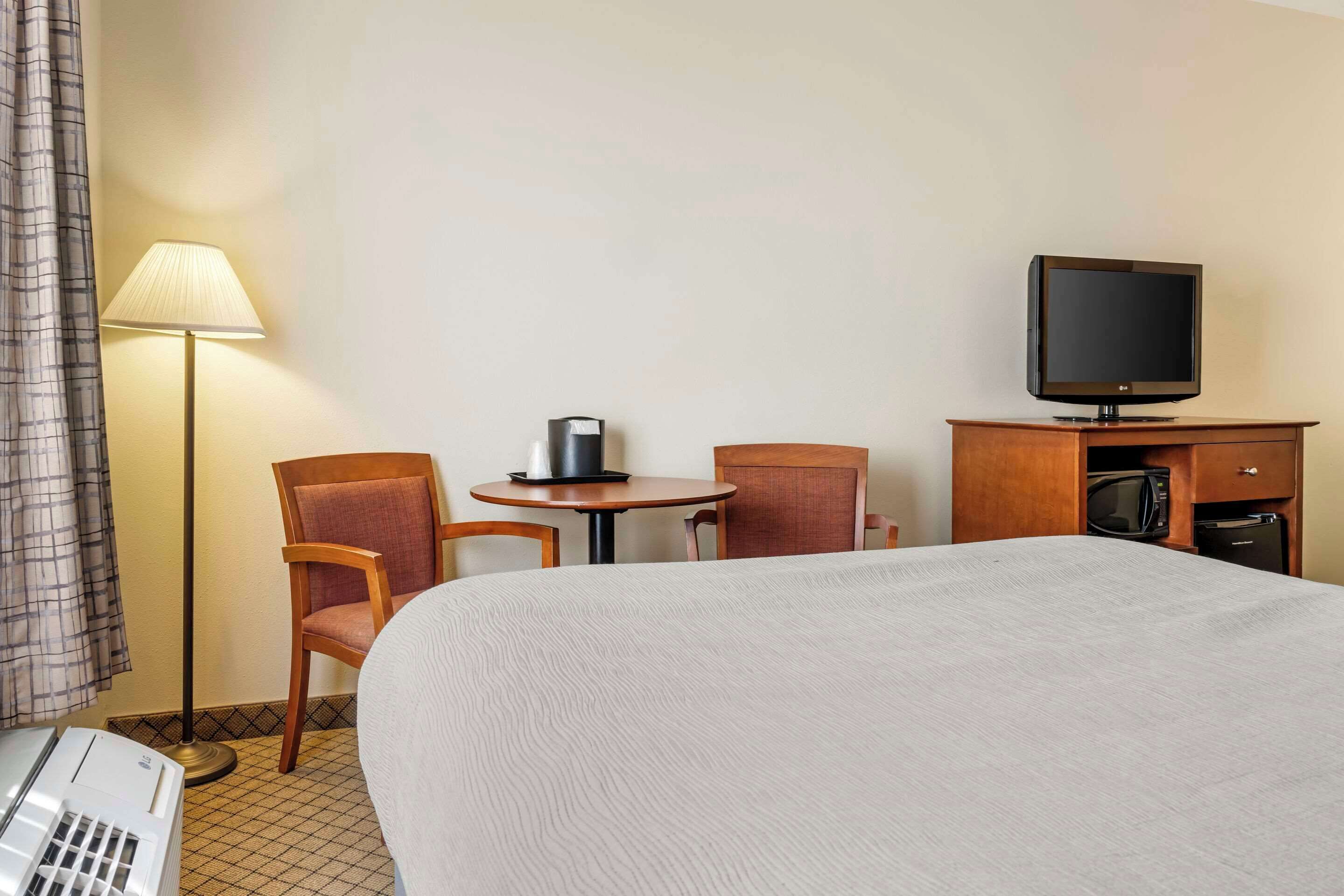 A hotel room with a bed, a desk with a computer, a TV, a lamp, and a chair.