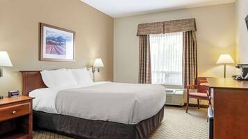 A hotel room with a bed, bedside tables, a desk, a chair, a window with curtains, and a wall-mounted picture.
