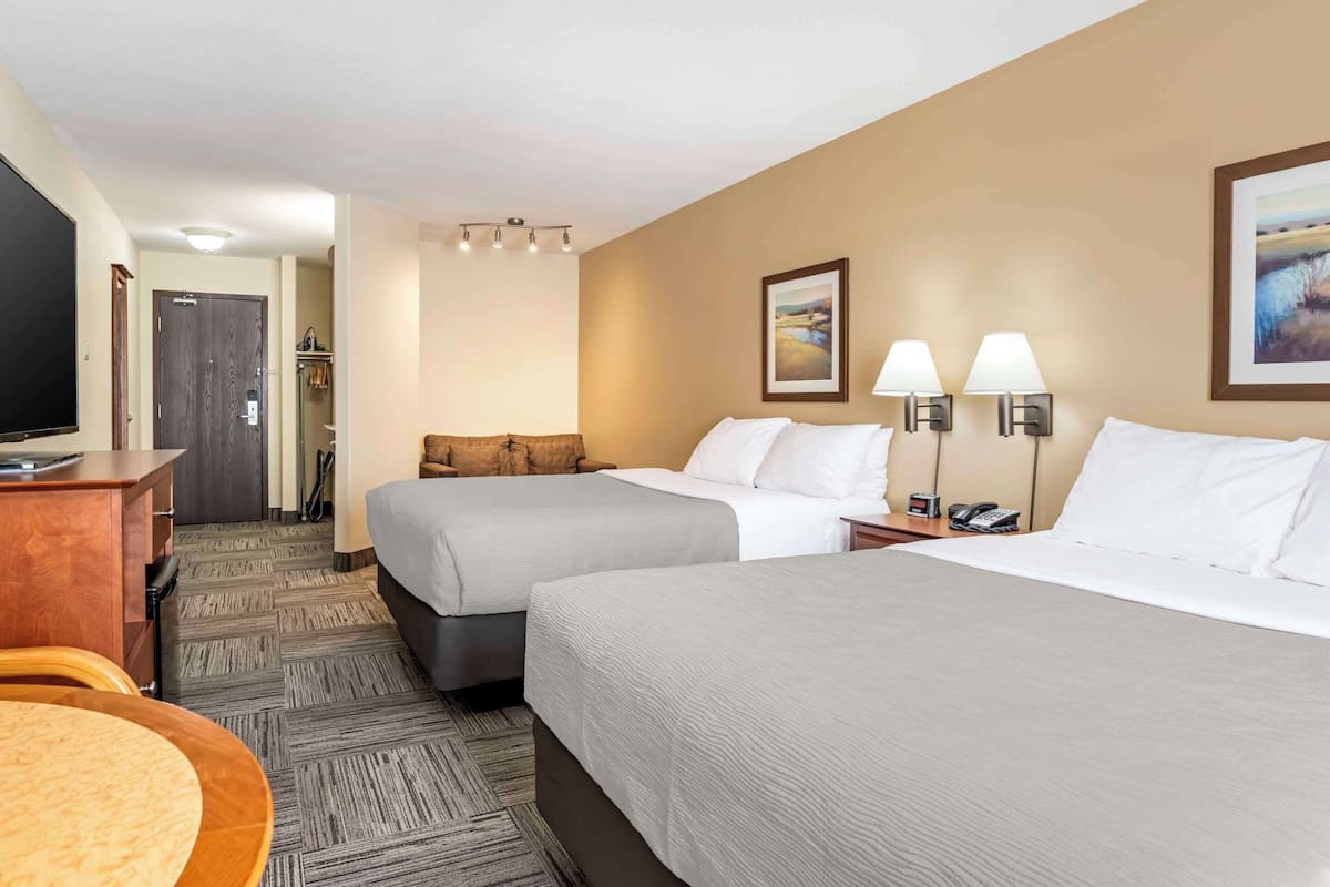 A hotel room with two beds, a desk, a TV, and a bathroom visible in the background.