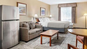 A hotel room with a bed, a sofa, a small table, a refrigerator, and two wall-mounted lamps.