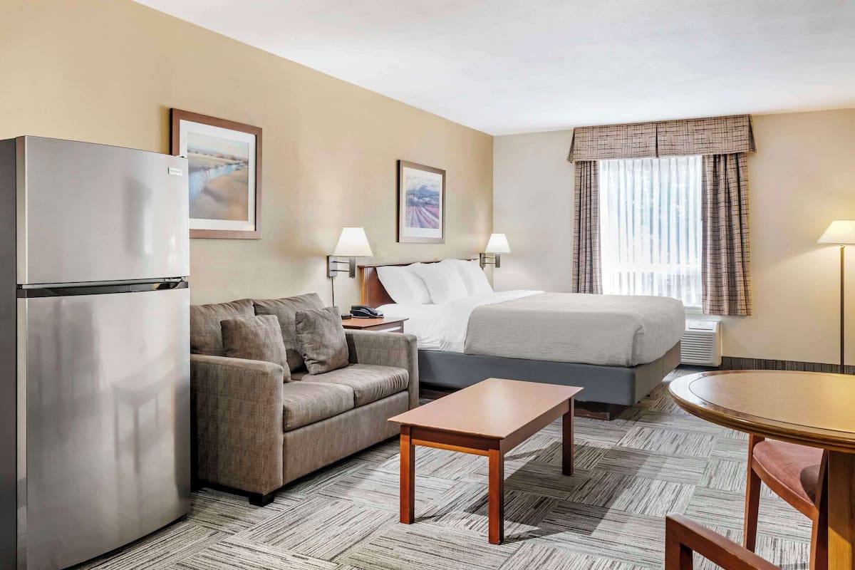 A hotel room with a bed, a sofa, a small table, a refrigerator, and two wall-mounted lamps.