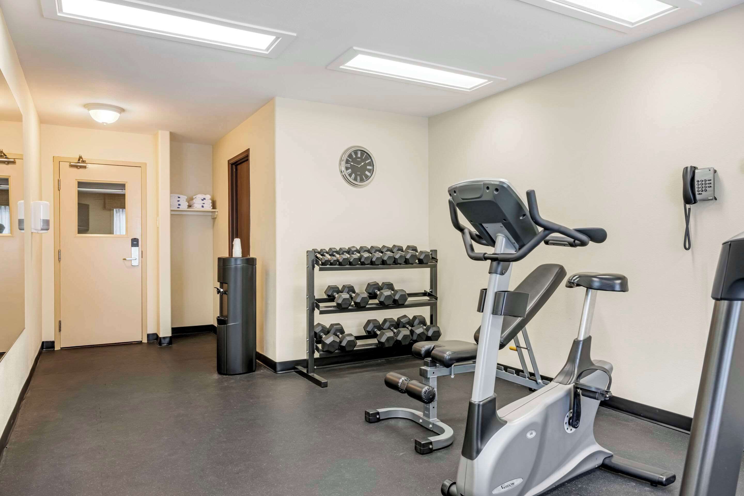 Una palestra con attrezzature per esercizi, un porta pesi, una sveglia e un telefono appesi al muro.