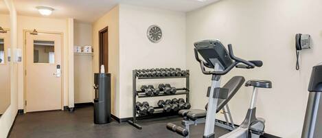Una palestra con attrezzature per esercizi, un porta pesi, una sveglia e un telefono appesi al muro.