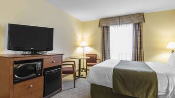 Una habitación de hotel con una cama, televisión, microondas, una mesita y una silla.