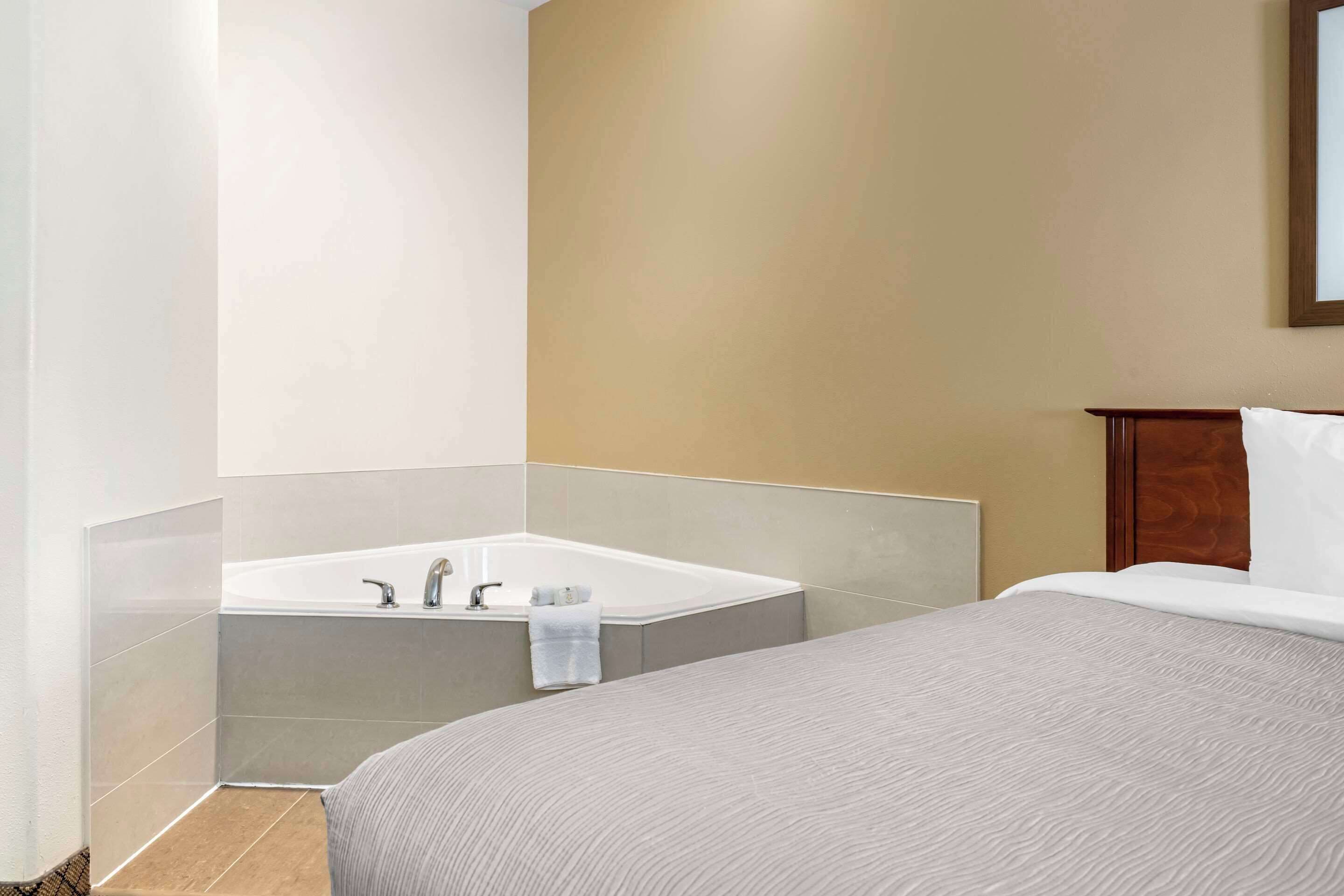 Habitación de hotel con una cama grande, baño separado con bañera y cabecero de madera.