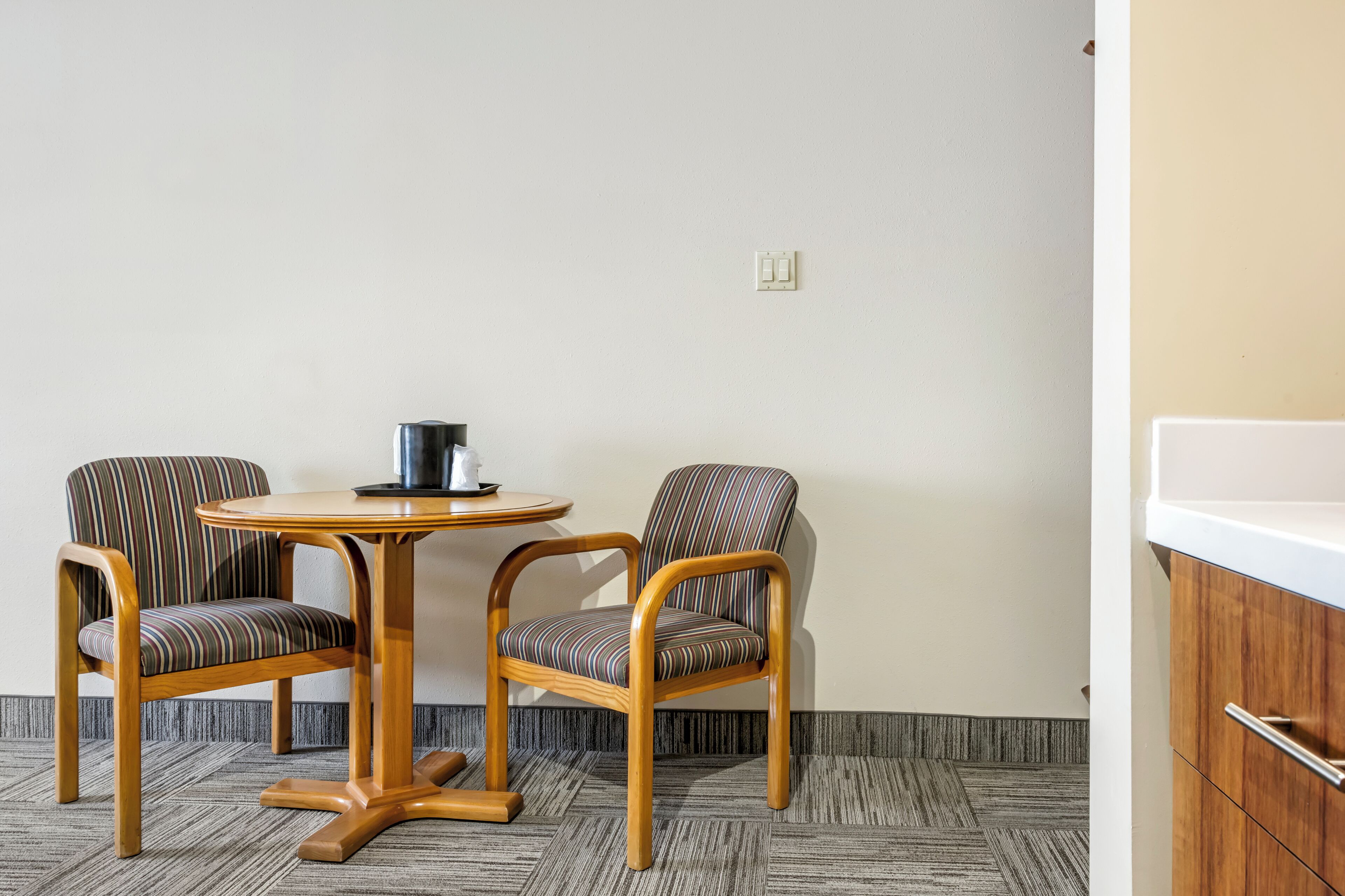 Une petite pièce avec deux chaises à rayures, une table ronde en bois et un évier blanc.