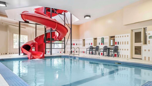 An indoor swimming pool with a red spiral slide, a seating area with chairs, and a tiled floor.