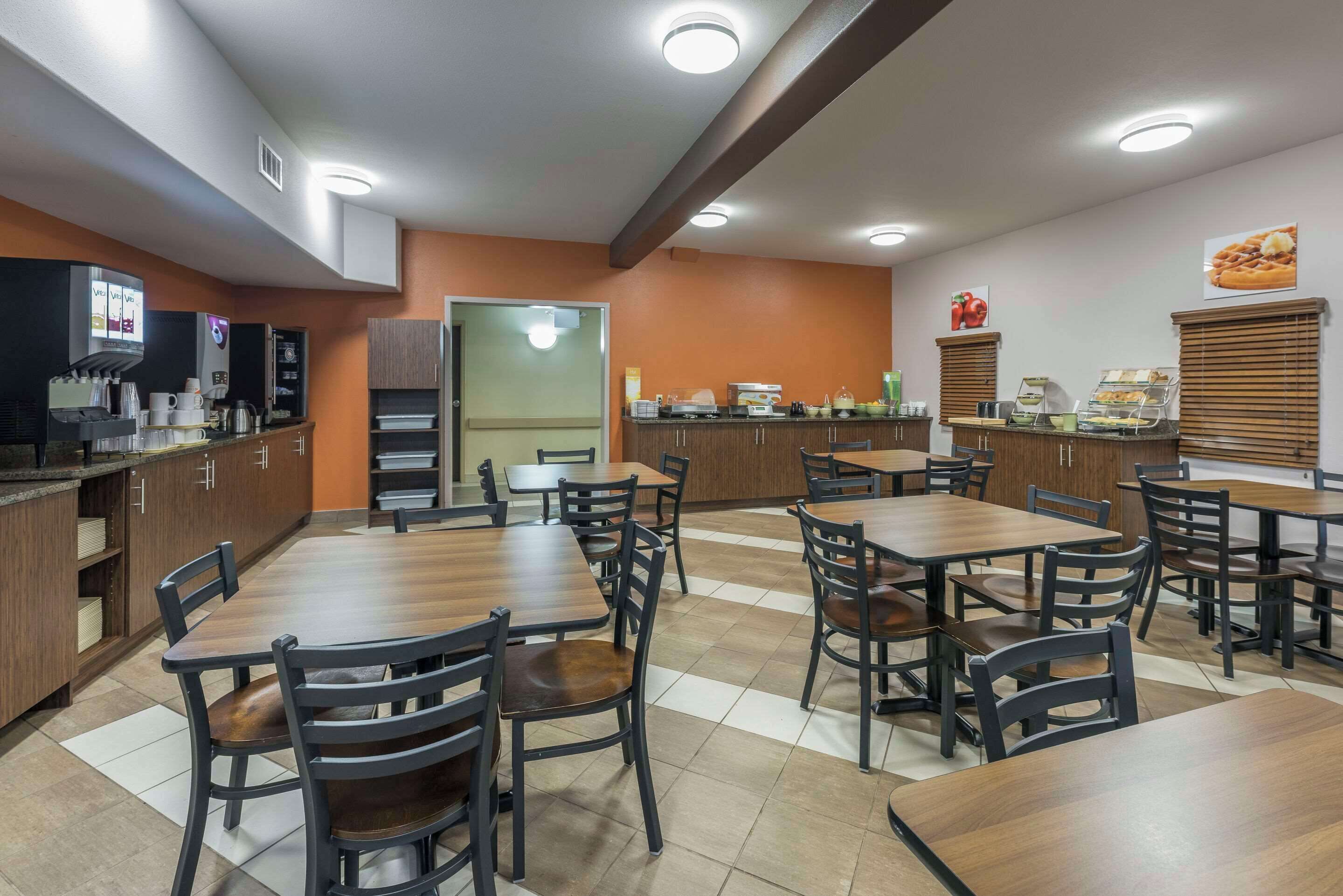 Um restaurante com várias mesas e cadeiras, uma área de cozinha e um balcão com vitrines de comida.