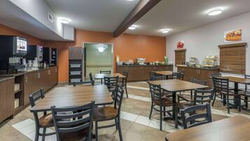 Um restaurante com várias mesas e cadeiras, uma área de cozinha e um balcão com vitrines de comida.