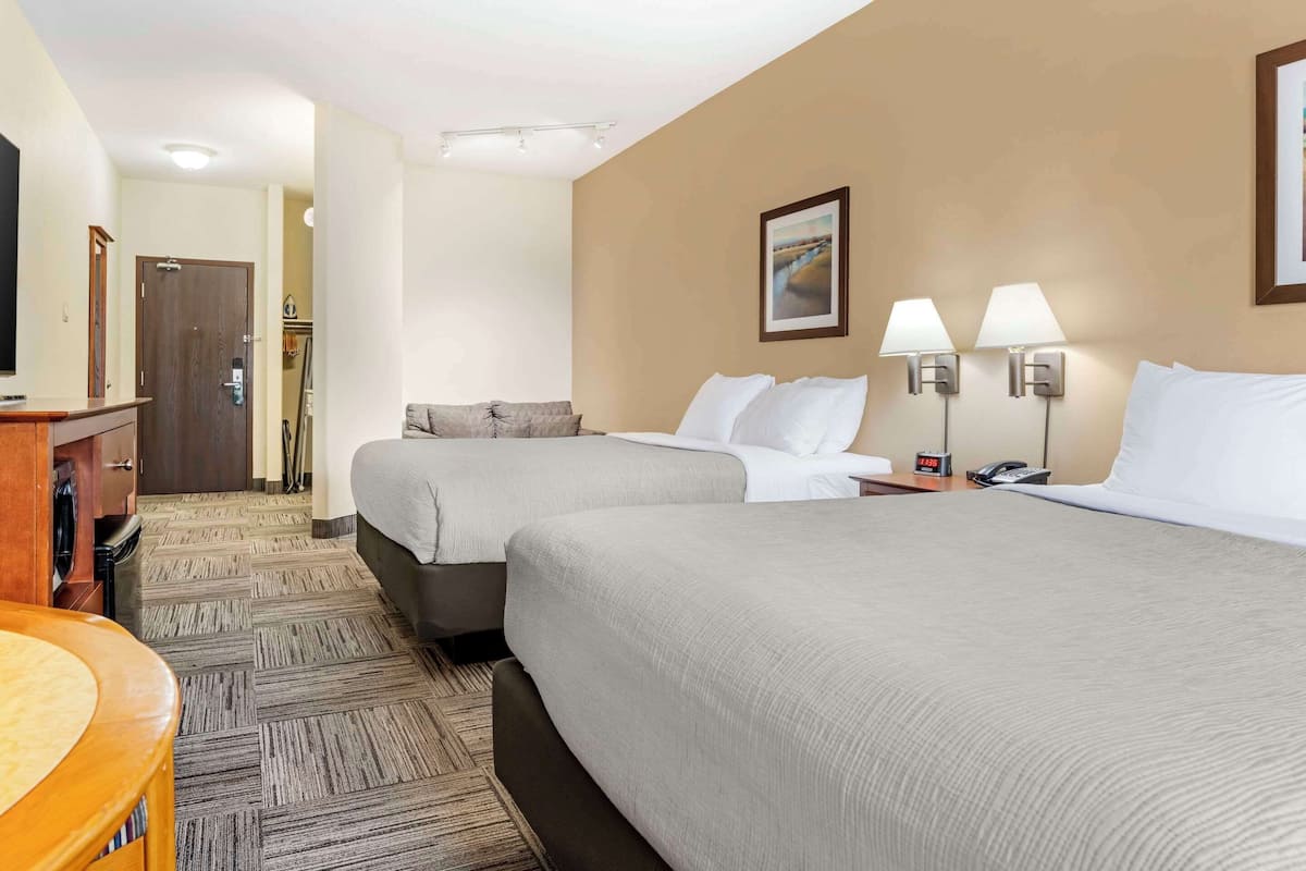 A hotel room with two beds, a desk, a chair, a TV, and a painting on the wall.