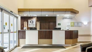 A reception desk with a sign reading 'Quality by Choice Hotels,' a wooden counter, a reception area, and a glass door entrance.