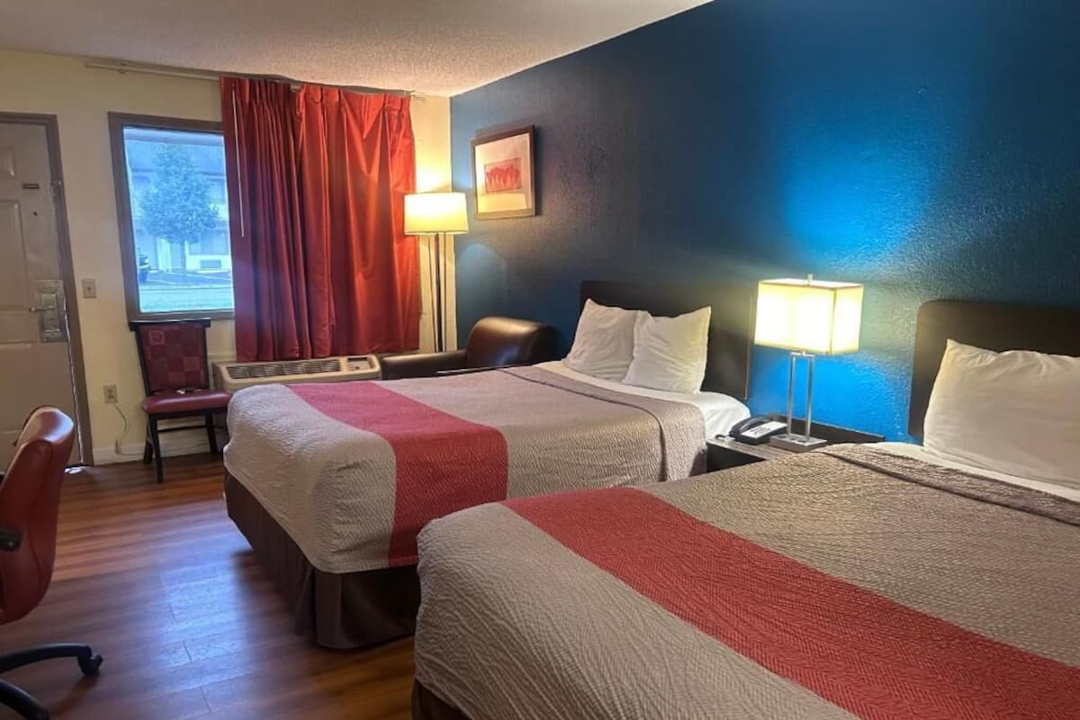 Hotellihuone, jossa on kaksi sänkyä, työpöytä, tuoli, televisio ja ikkuna, jossa on verhot.