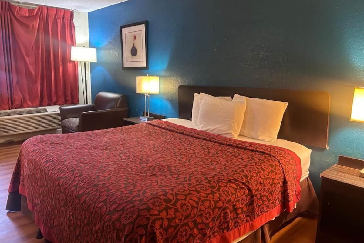 Hotellihuone, jossa on suuri sänky, kaksi yöpöytälamppua, tuoli, työpöytä ja ikkuna, jossa on verhot.