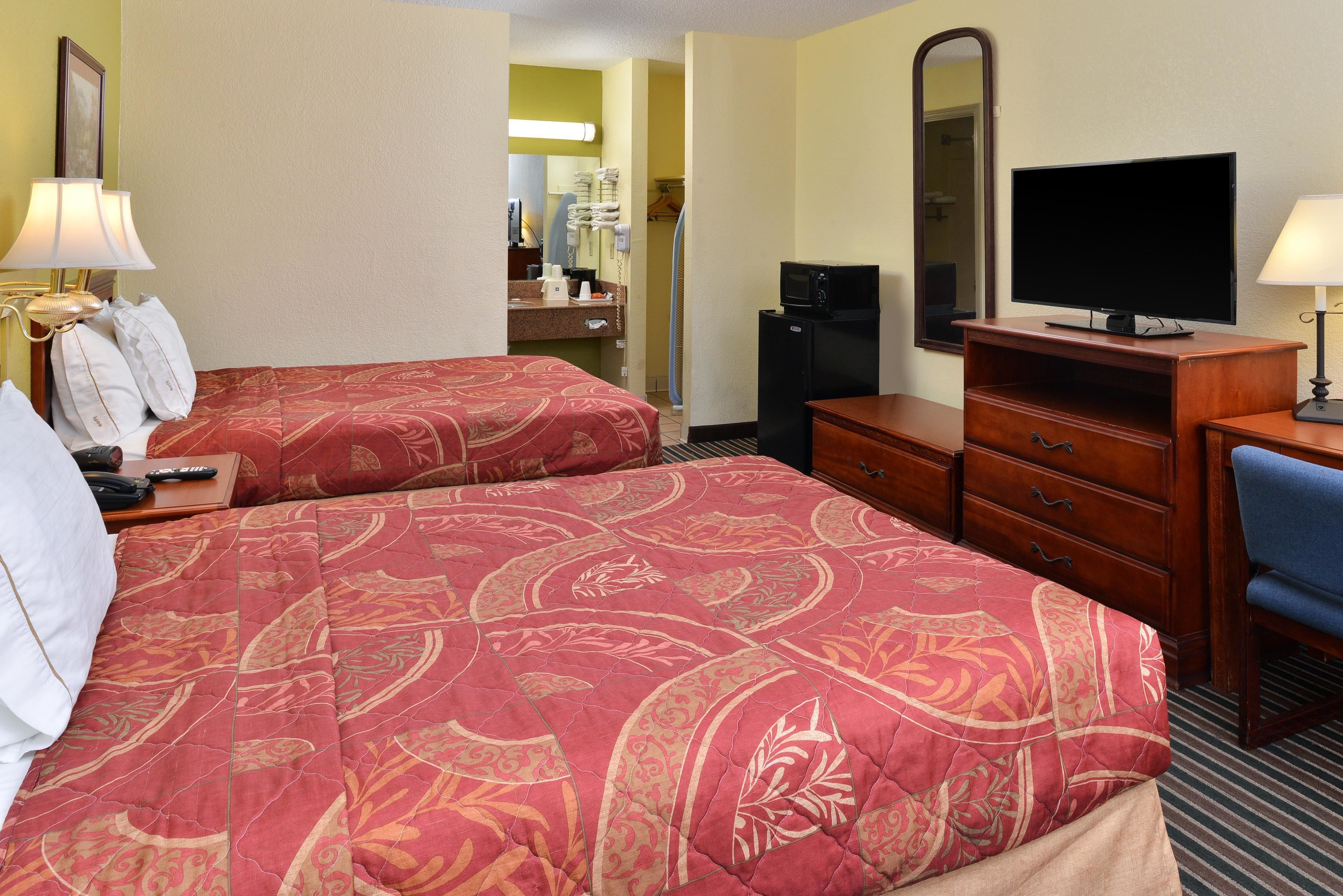 A hotel room with two beds, a TV, a desk, and a mirror.