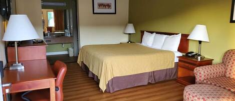 A hotel room with a bed, desk, chair, and a small kitchenette.