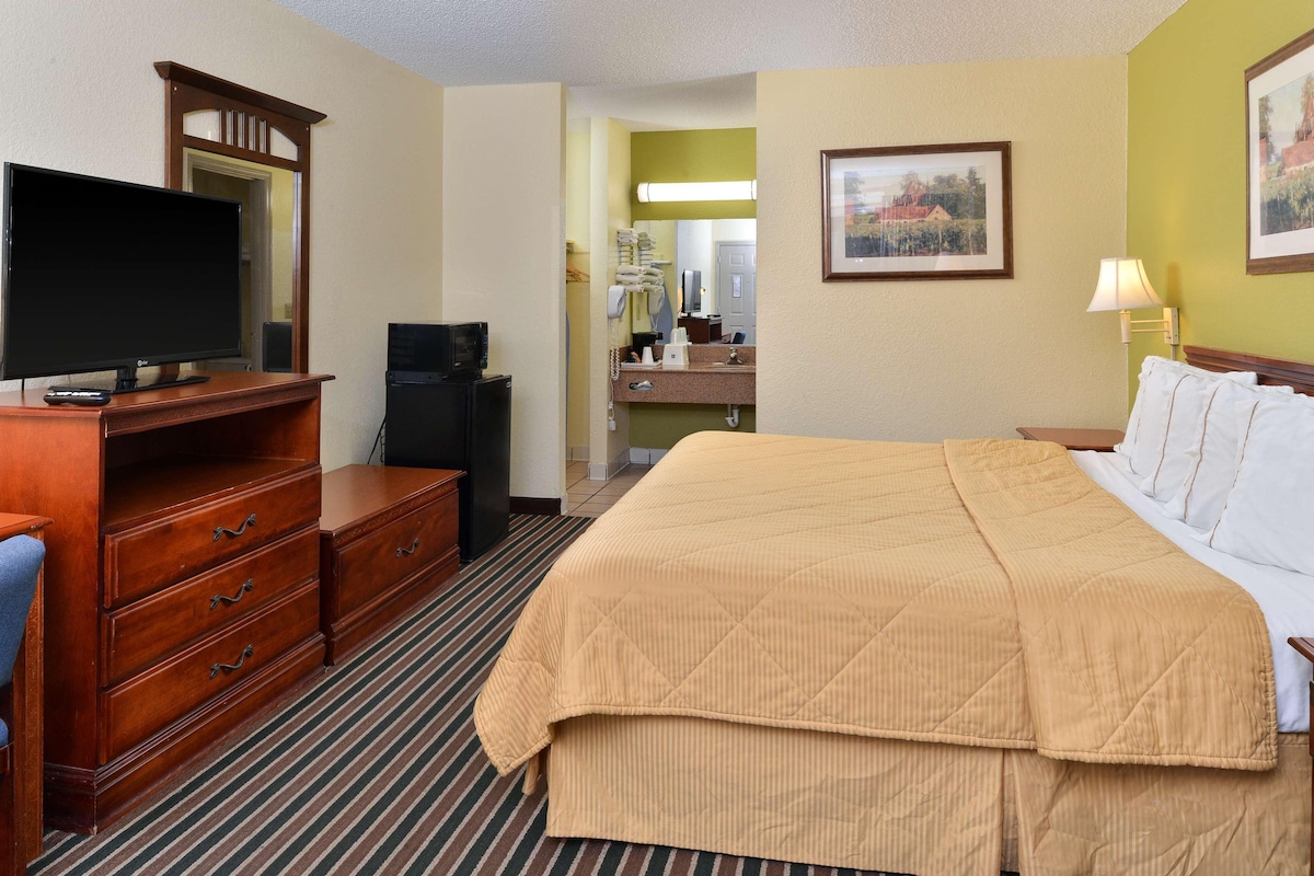 A hotel room with a large bed, wooden dresser, flat-screen TV, and a desk with a computer.