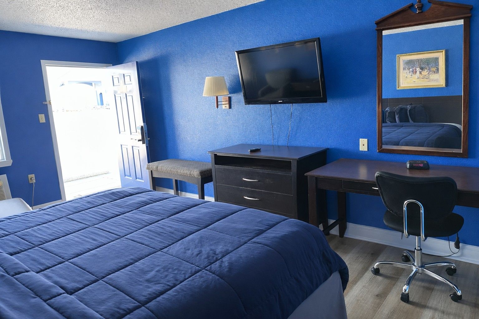 A hotel room with a large bed, a desk with a chair, a television, and a window with a view.
