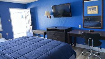 A hotel room with a large bed, a desk with a chair, a television, and a window with a view.