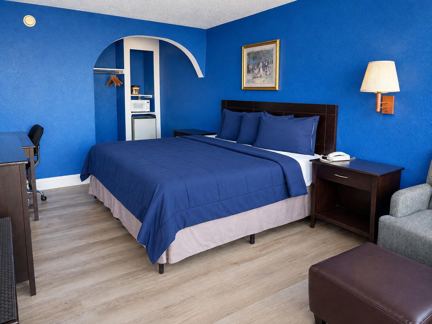 Ein Hotelzimmer mit Bett, Schreibtisch, Stuhl, Lampe und Kleiderschrank.
