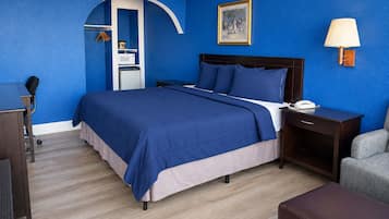 A hotel room with a bed, a desk, a chair, a lamp, and a wardrobe.