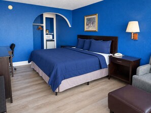 A hotel room with a bed, a desk, a chair, a lamp, and a wardrobe. - Apollo Lodge and RV Park (Fairfield)