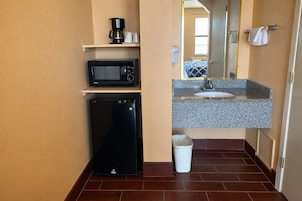 Un baño pequeño con microondas, refrigerador, lavamanos y un cubo de basura.