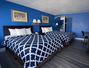 A hotel room with two beds, each with a patterned bedspread, a desk with a chair, and a lamp.