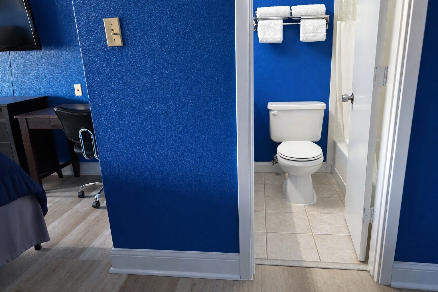A hotel room with a blue accent wall, a white toilet, and a small desk with a chair.