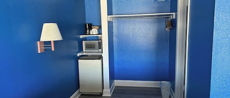 A compact kitchen with a microwave, kettle, and kettle holder on a shelf.