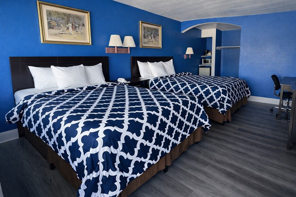 A hotel room with two beds, each with a patterned bedspread, a desk with a chair, and a lamp.