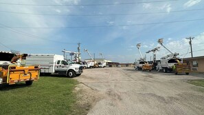 A parking lot with utility trucks and equipment, a building in the background, and a clear sky.