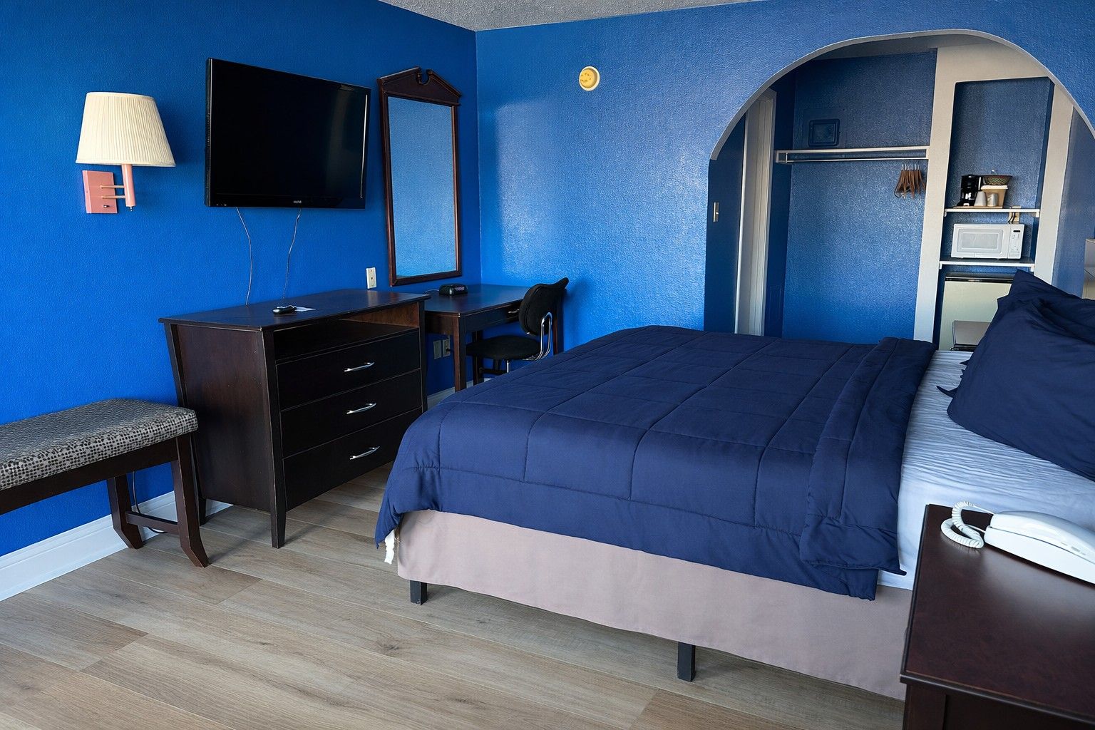 A bedroom with a bed, a dresser, a desk, a chair, a television, and a wardrobe.