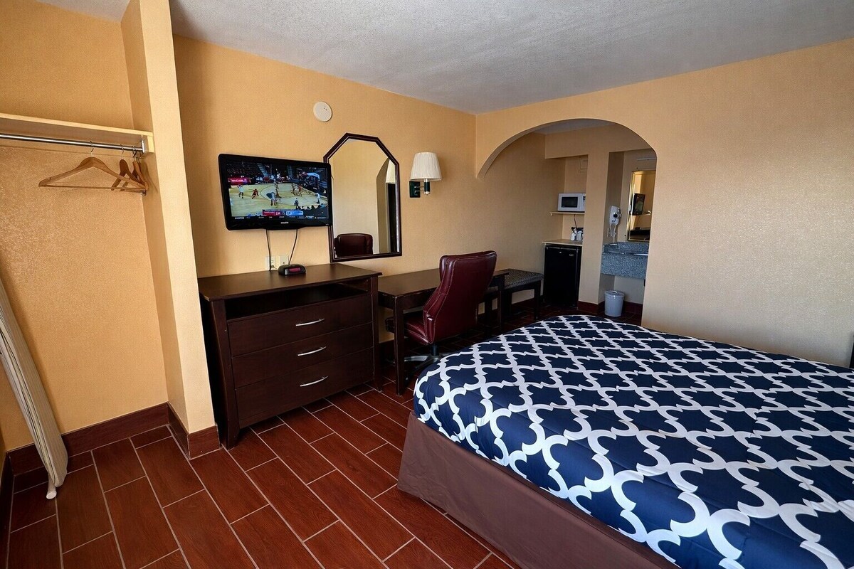 Una habitación de hotel con cama, escritorio, silla, televisor y espejo.