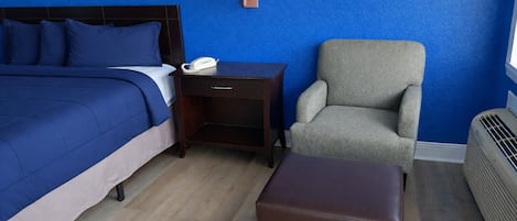 Quarto de hotel com cama, mesa de cabeceira, cadeira e aquecedor.